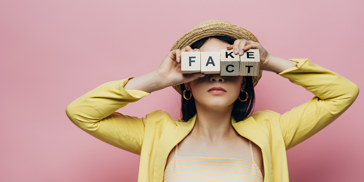 Femme tenant des cubes en bois devant le visage avec les mots faux et factuel, isolées sur du rose