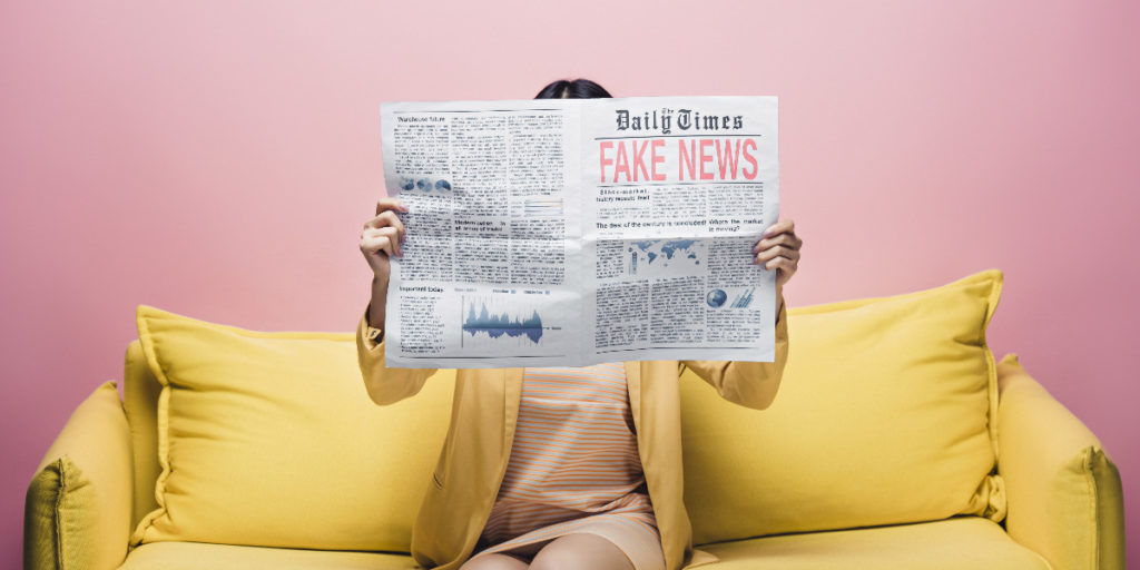 femme tenant un journal avec de fausses nouvelles devant le visage alors qu'elle est assise sur un canapé jaune isolée